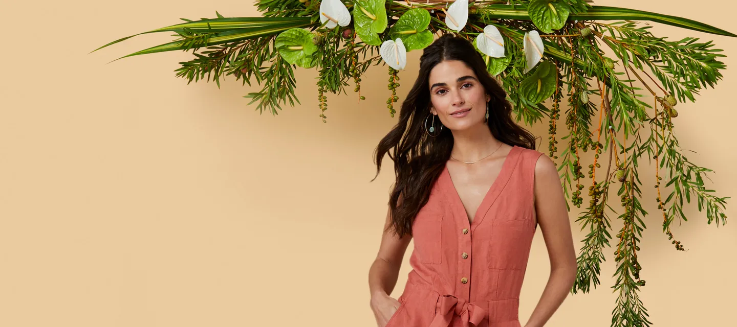 woman in a peach dress standing in front of a beige wall and green plant