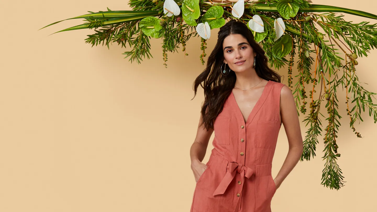 woman in a peach dress standing in front of a beige wall and green plant