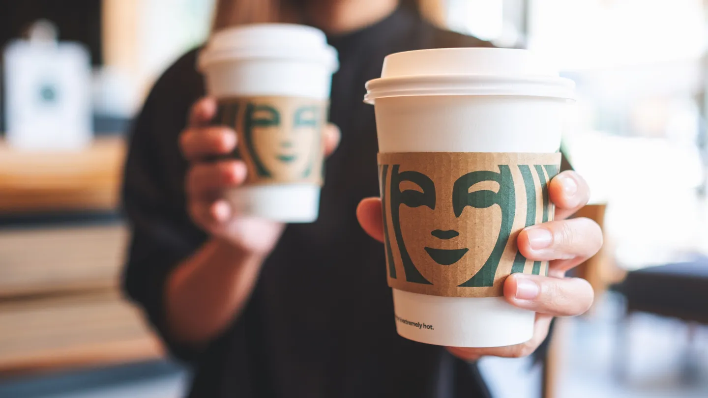 Person holding two coffee cups showing the Starbucks logo